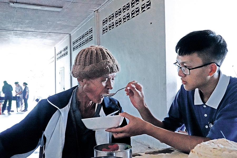 泰北熱水塘安養中心段興旺爺爺已經沒有牙齒，來自臺灣的大學生志工陳弈亘（右）一匙匙協助他進食