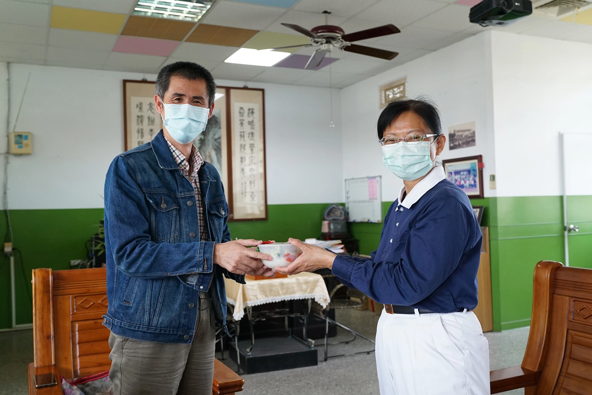 海埔國小校長施榕鑫從志工劉妙玲手中接過平安吊飾與志工用心製作的素食便當