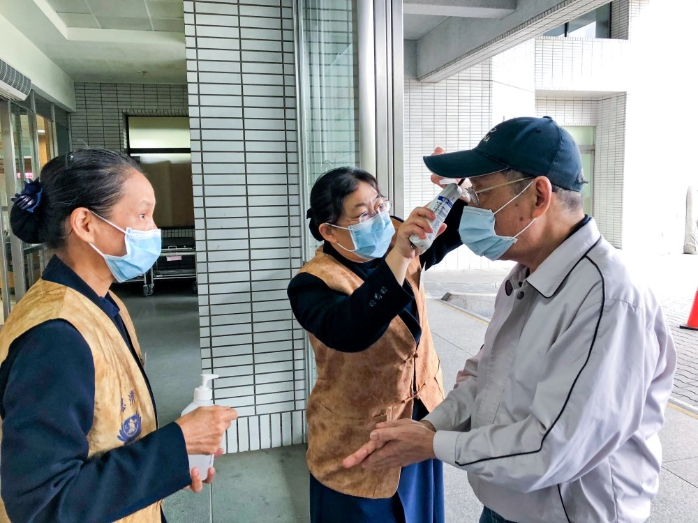 醫療志工在門診大廳協助民眾測量體溫與手部消毒。