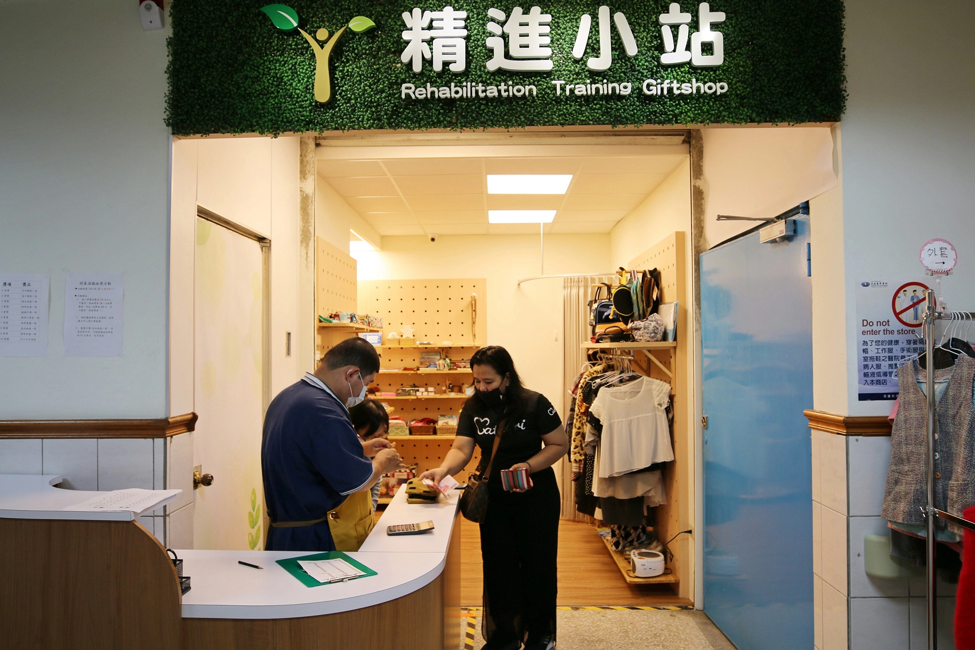 精進小站草綠色的招牌上有象徵「新芽」的圖騰，代表著眾人的愛心灌溉下，學員們的人生旅程也可以持續成長茁壯；內部則是增加了舒適的試衣間，以及暖色調的木櫃，擺放學員們精心製作的手工藝品及二手衣物。
