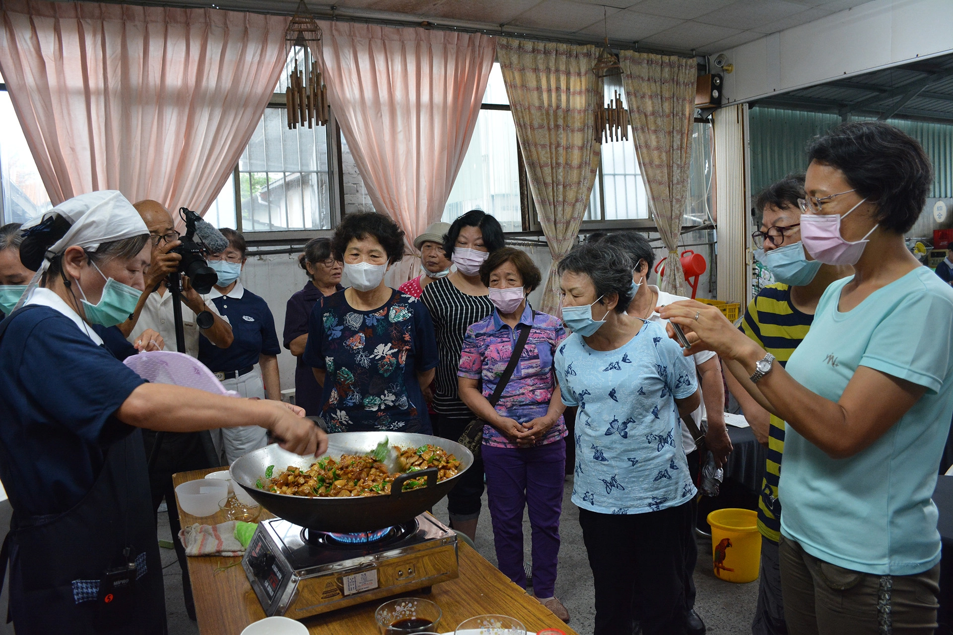 環保站飄菜根香，陳明足師姊示範素食料理是「三杯杏鮑菇」，吸引大家專注的目光，紛紛以手機錄影或做筆記。