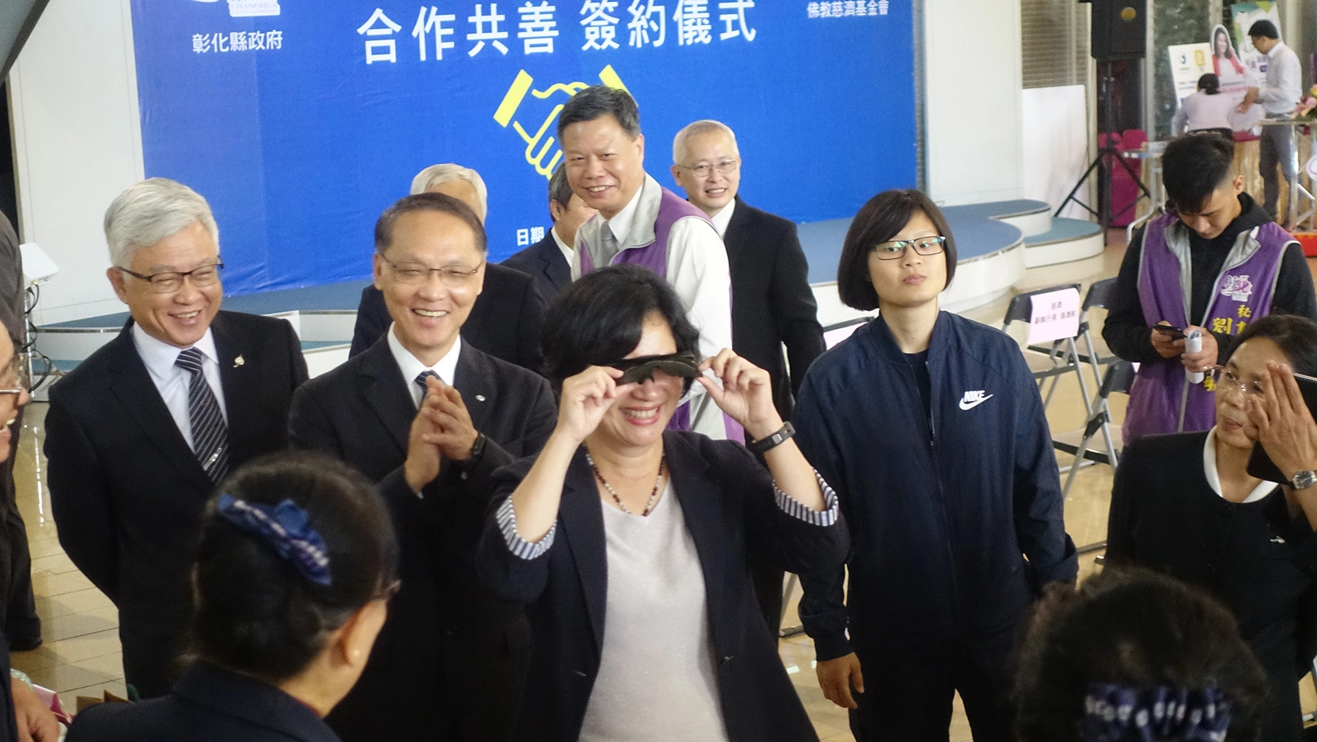 顏博文執行長介紹慈濟用寶特瓶製成的生活用品，王惠美縣長立刻試戴太陽眼鏡。