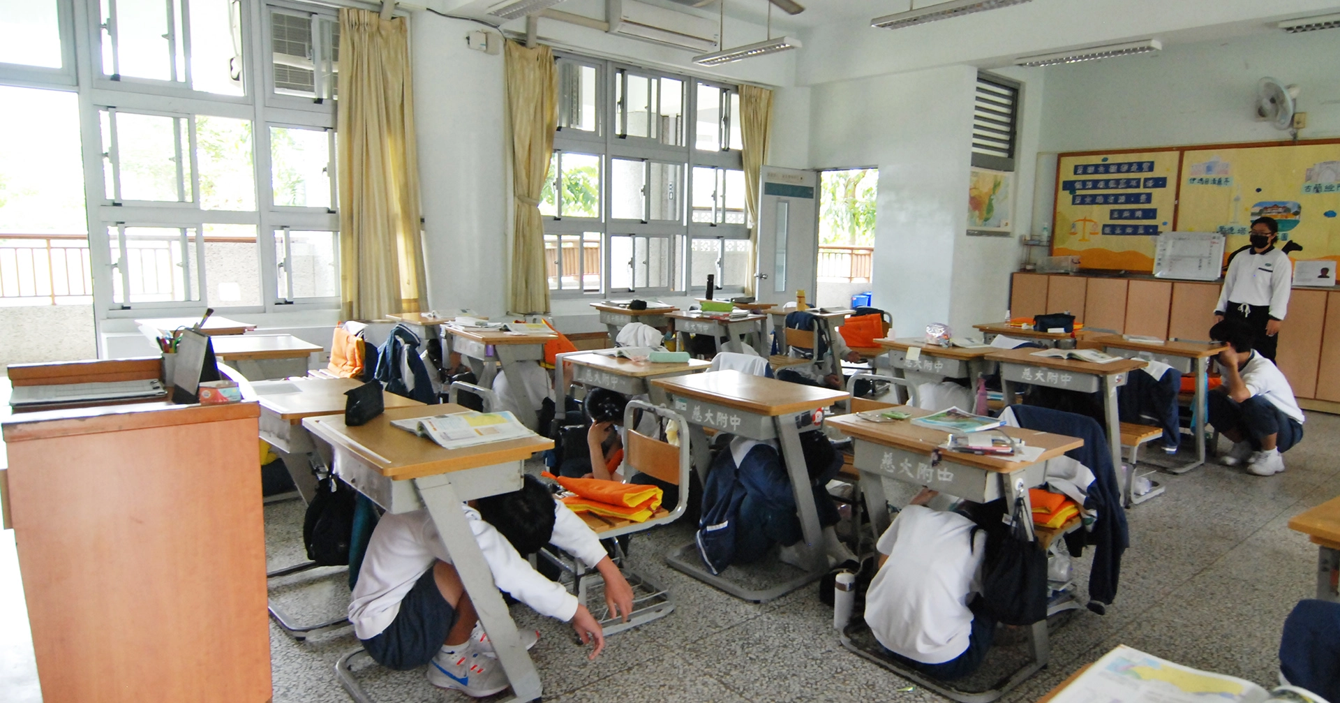 慈大附中全校師生進入地震模擬情境，師生躲在桌下、柱旁或牆邊，等地震稍歇後，由師長引導學生快速至運動場集合。