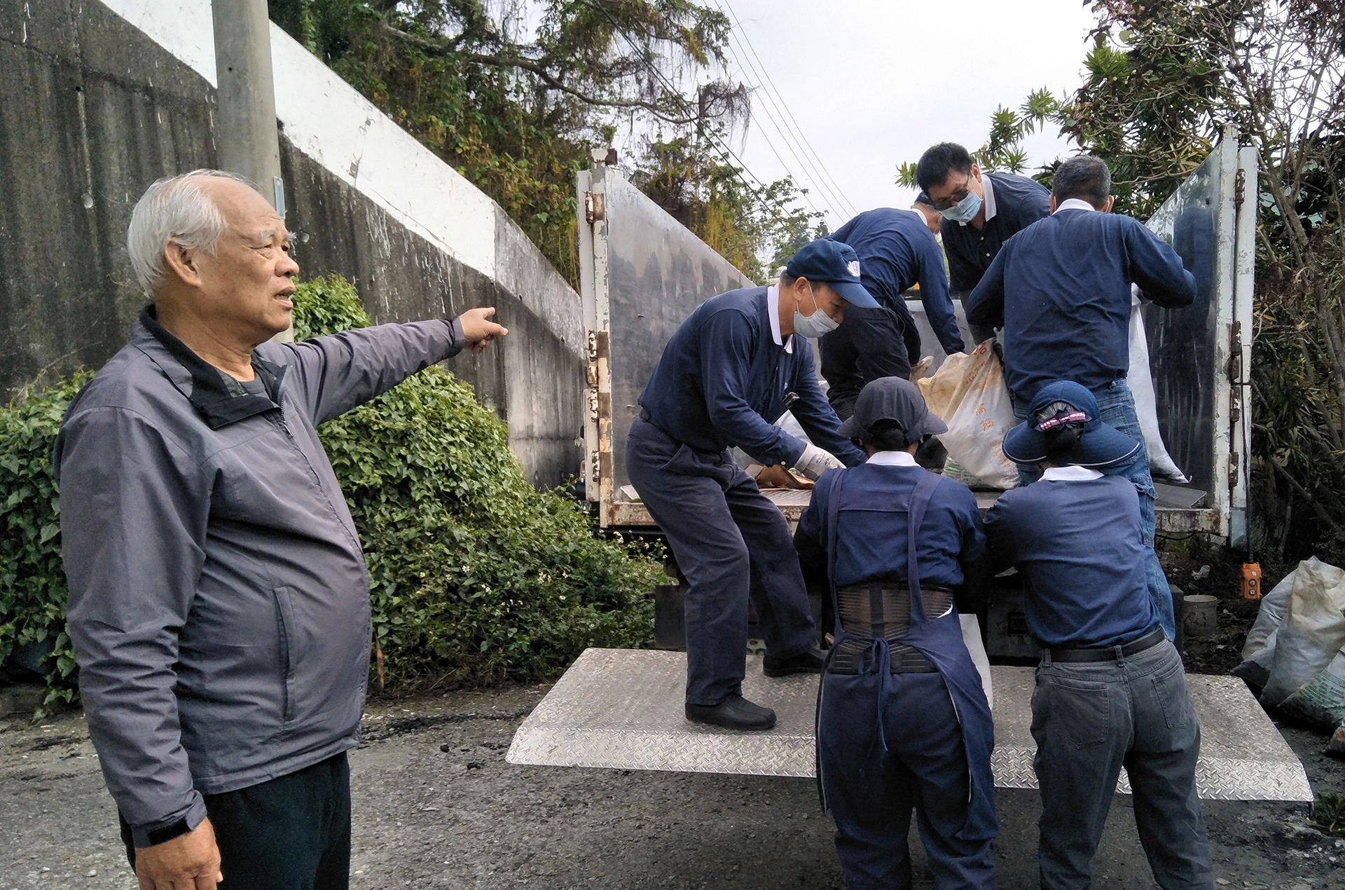 草屯鎮公所清潔隊協助載運清理出來的廢棄物，洪智捷里長(左)親臨現場關懷，里長夫人也協助清掃。