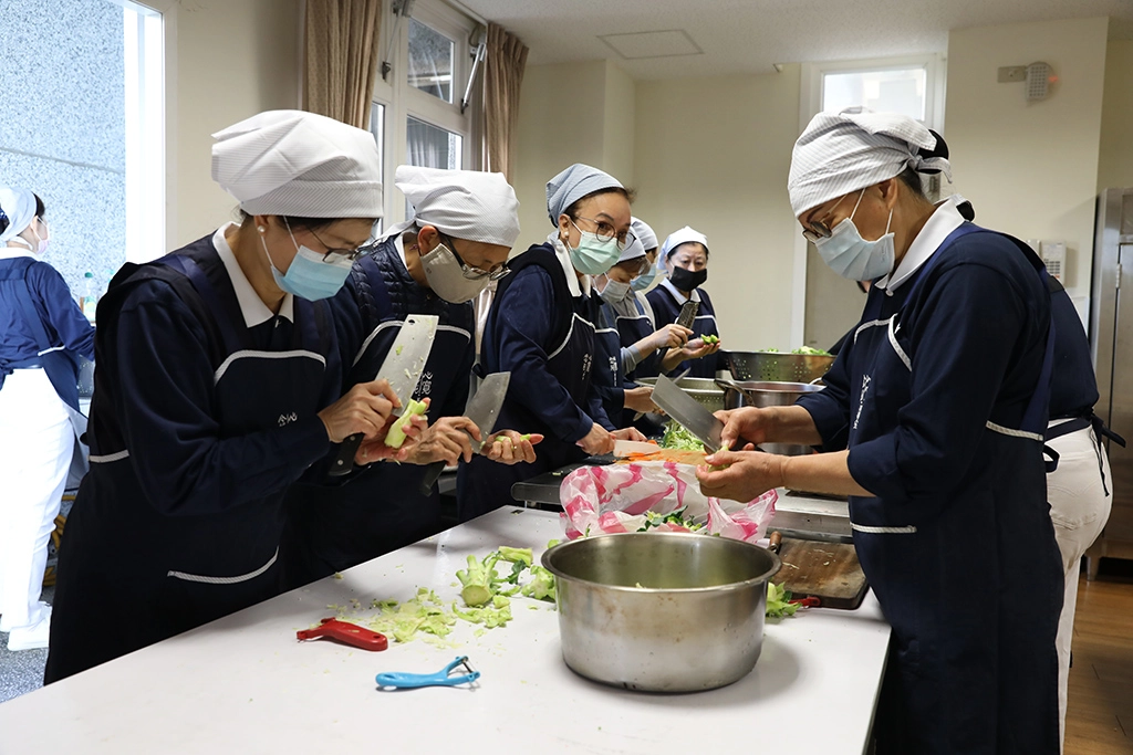 卅位志工就從洗菜、切菜、煮食到打菜、裝便當，如同生產線般井然有序，大家懷著一份感恩及祝福的心，希望透過這份愛心為醫護人員打氣。