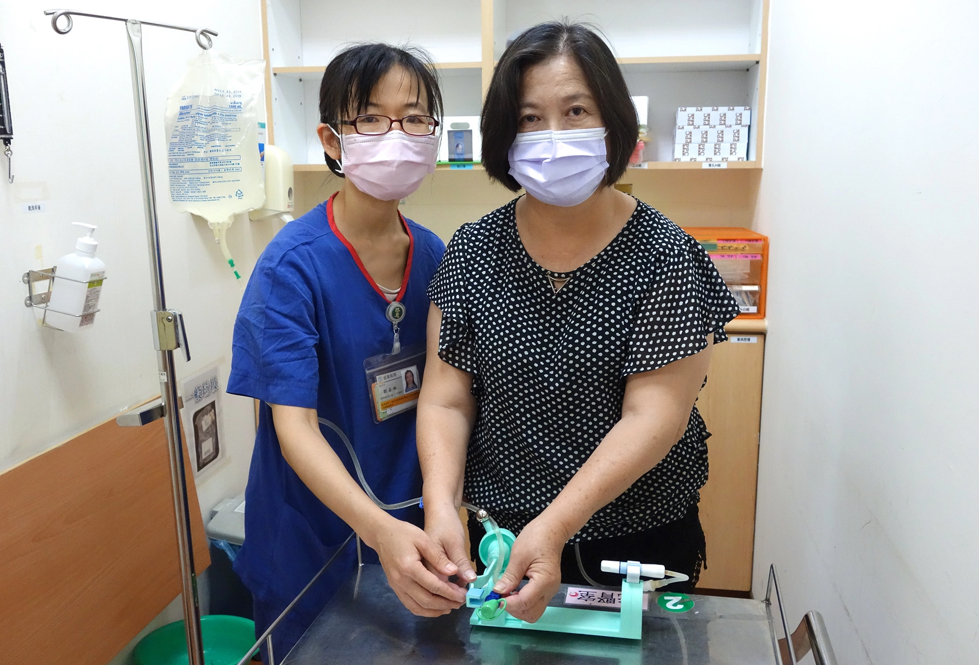 左邊人物為腹膜透析護理師劉嘉琳，右邊為洗腎病患，護理師指導病人如何使用腹膜透析接管固定輔助裝置