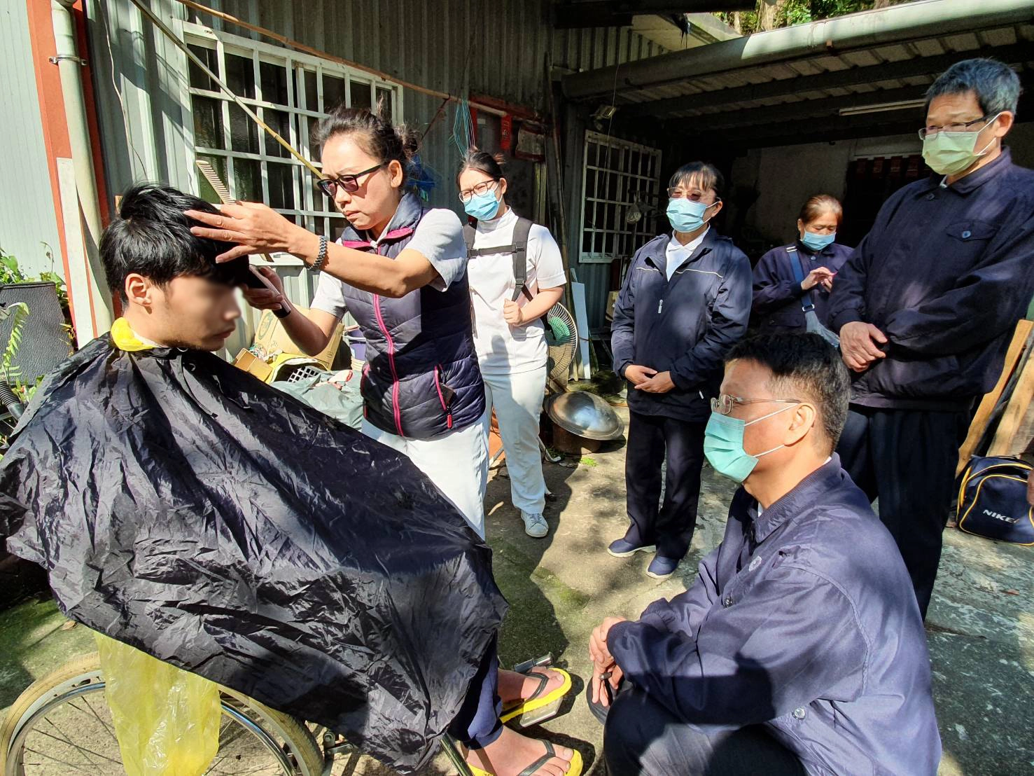 連進昌醫師（右）、蔡文方醫師（前蹲者）帶隊前往關懷案家賴先生的身心健康。黃惠芳師姊從旁協助義剪。