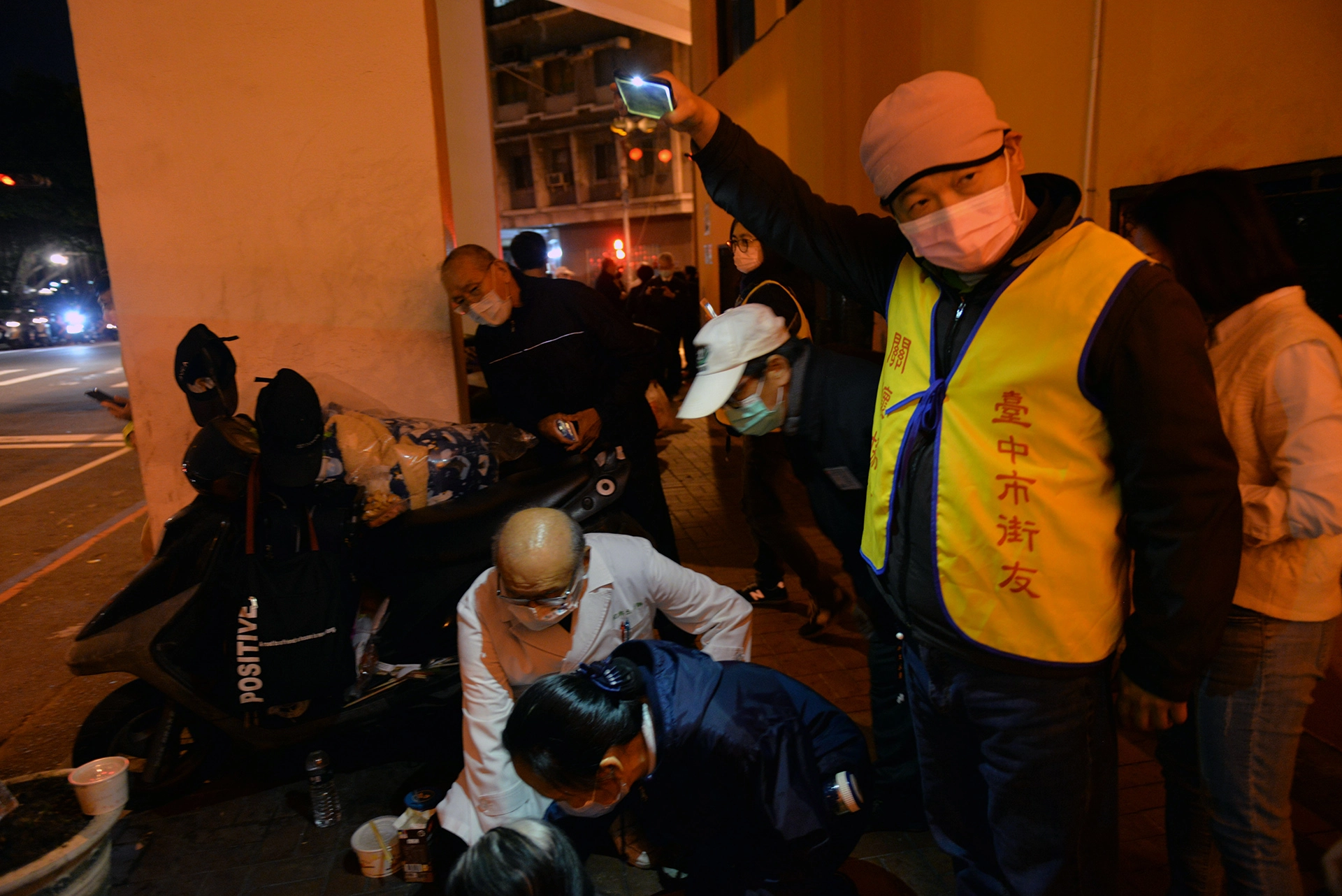 台中市街友關懷協會何志成理事長（右）用手機幫人醫會醫護人員照明。