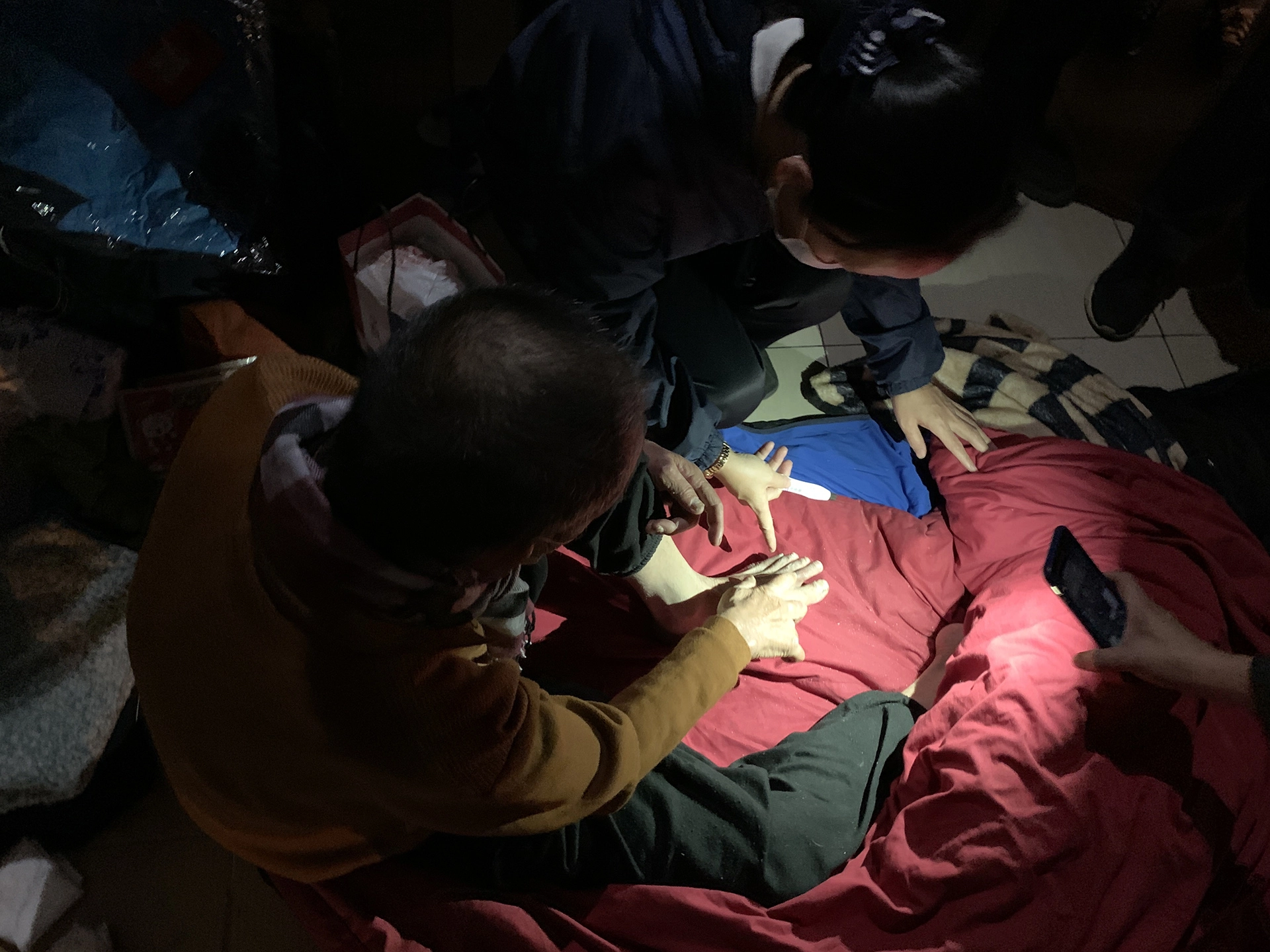 騎樓下必須依賴手機燈光的照射，人醫會的醫護人員才能清楚看到街友腳上凍裂的傷口。