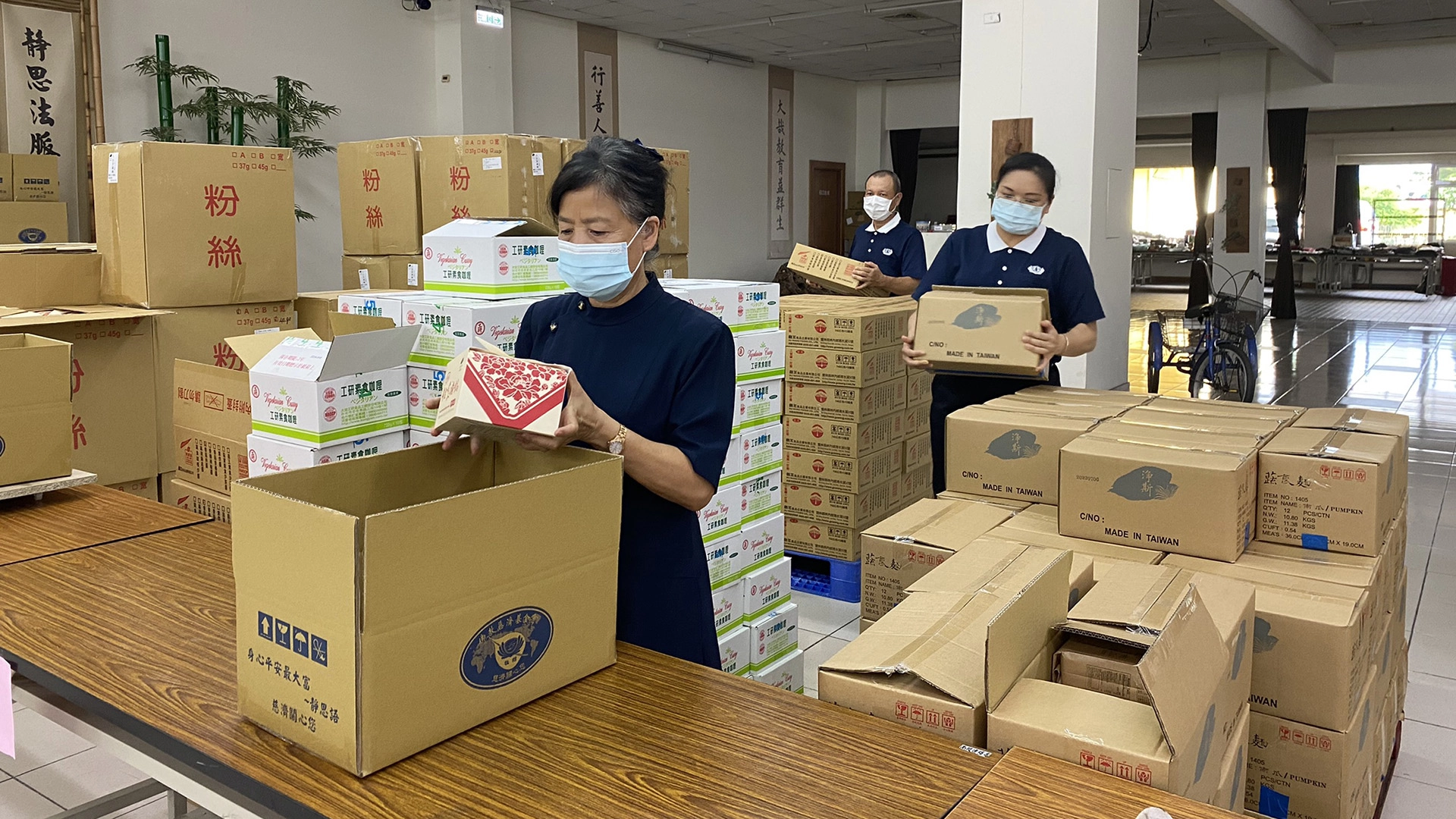 慈濟結合南投縣政府捐贈2062戶弱勢學童家庭暑期安心生活箱、健康蔬果箱，7月9日上午在南投聯絡處進行包裝工作。