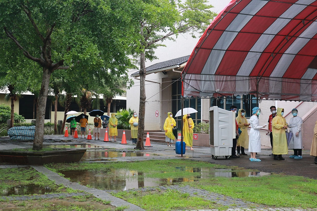 雨勢不斷，接受快篩的群眾穿著雨衣、撐著傘，由現場同仁指揮，依序完成排隊、掛號、篩檢，最後等候報告。