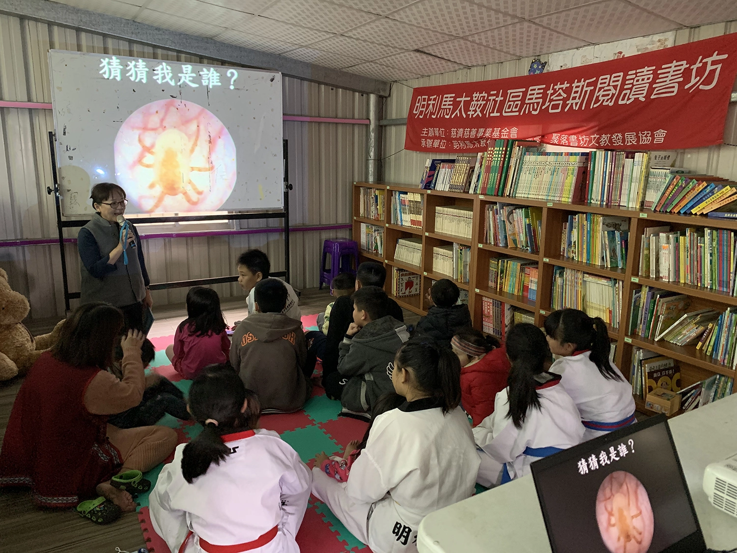 聚落書坊理事長王緯華說故事〈塵螨丁丁搬家記〉，不只孩童聽得津津有味，窗戶旁的家長也聚精會神專注聽。(攝影：徐靖雯)
