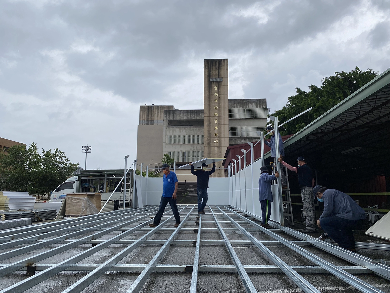 5月30日在松柏育樂中心搭建篩檢組合屋，營包商雨中施工希望趕緊搭建完成。(攝影：吳珮婕)
