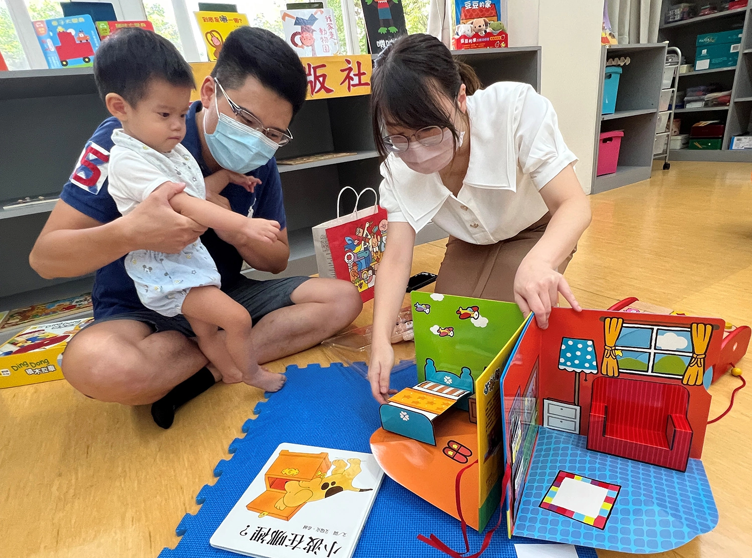 1歲10個月的恩恩，加入早療中心的課程後肢體動作與各項發育已經漸漸有了進步，也能認真聽故事。爸爸(左2)最大的願望是想帶他去日本迪士尼樂園好好地玩樂。(圖高雄市社會局提供)