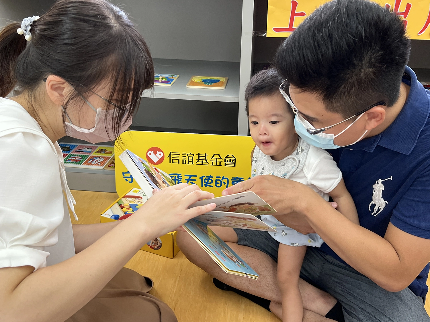 1歲10個月的恩恩，加入早療中心的課程後肢體動作與各項發育已經漸漸有了進步，也能認真聽故事。爸爸(右)最大的願望是想帶他去日本迪士尼樂園好好地玩樂。(圖高雄市社會局提供)