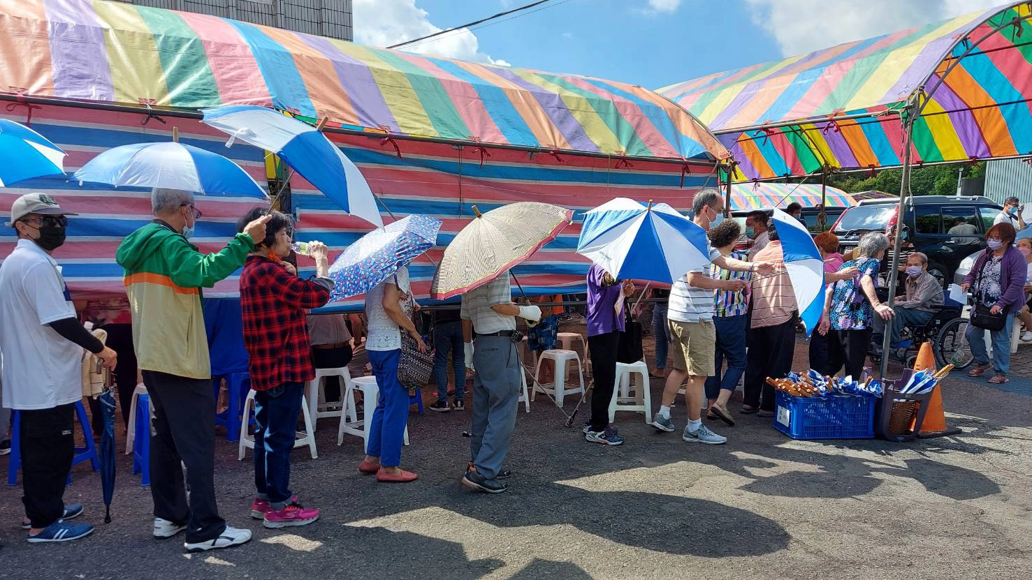 慈濟沙鹿聯絡處提供所有遮陽傘具(圖右地上置放傘箱)供排隊民眾防曬使用。