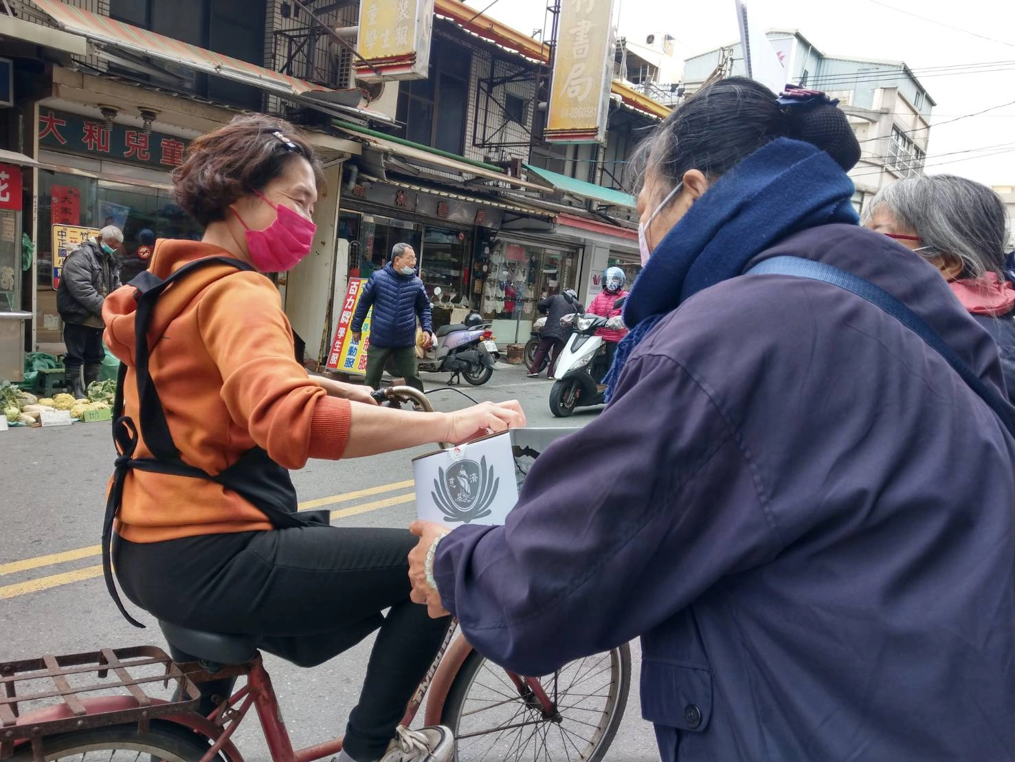 愛心商店的老闆娘得知志工在定點募愛，專程騎單車來投愛心。(圖為慈濟基金會提供)