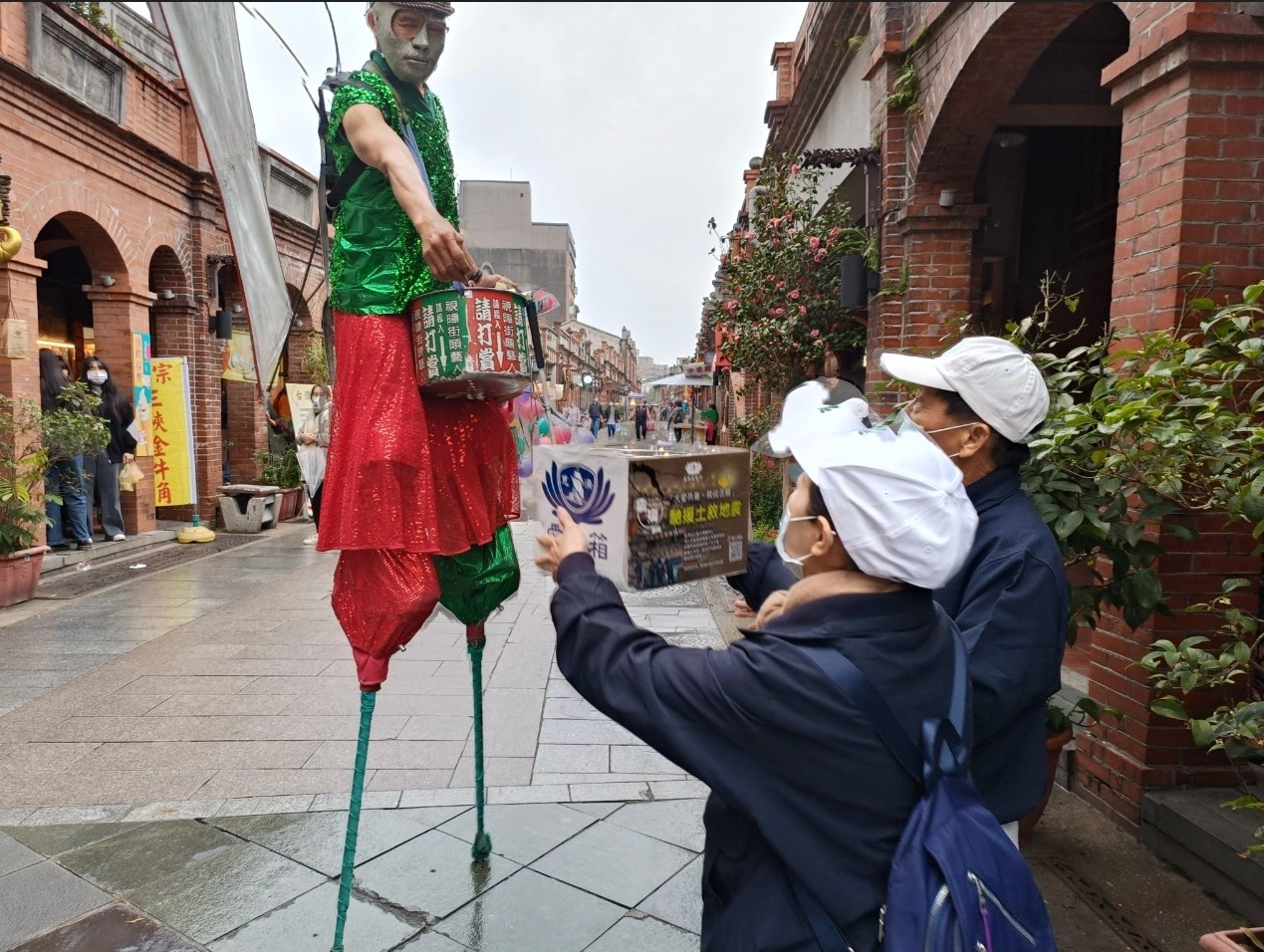 在三峽老街，一位街頭藝人在表演完畢後，踩著高蹺來到慈濟人面前，將他辛苦表演的賞金投入捐款箱。