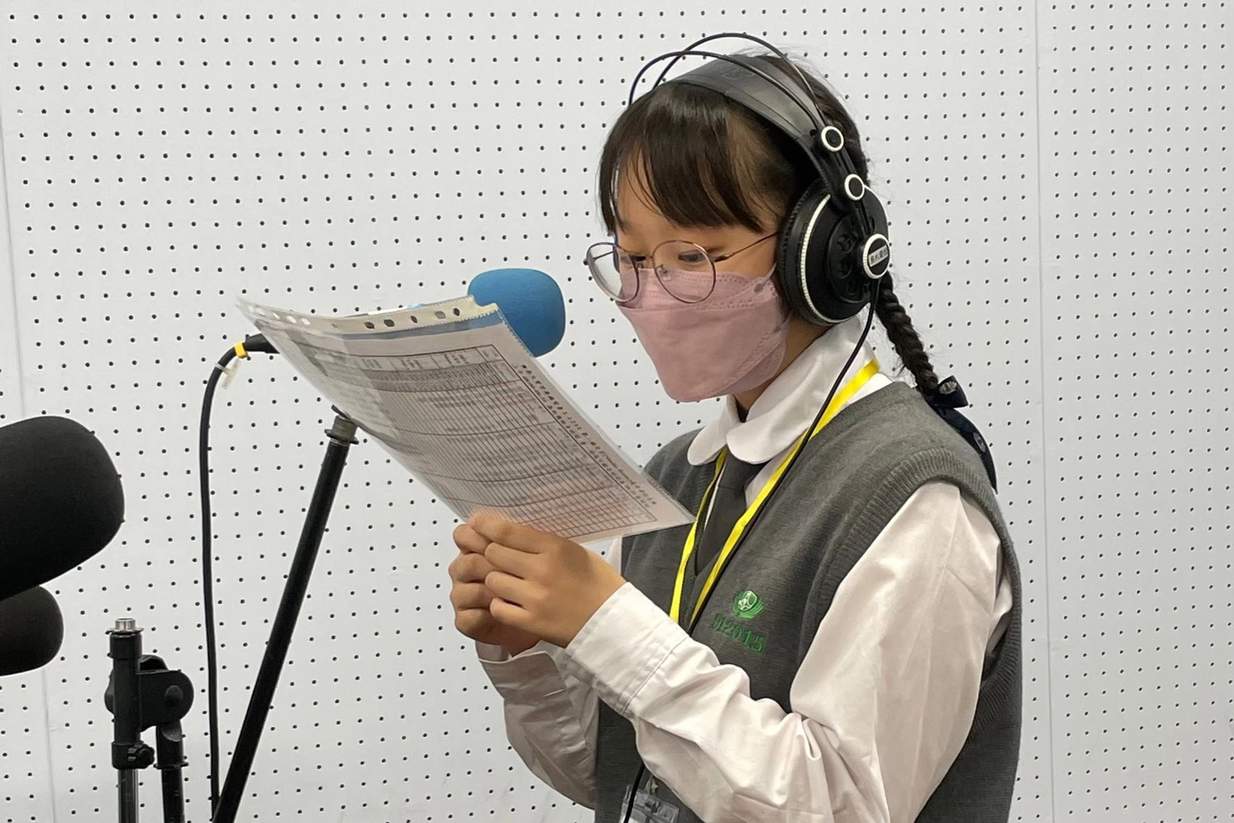 臺南慈中高三黃映瑜同學走進攝影棚、拿著麥克風、聽著導播的倒數和看著眼前的逐字稿，嘗試播報新聞。
