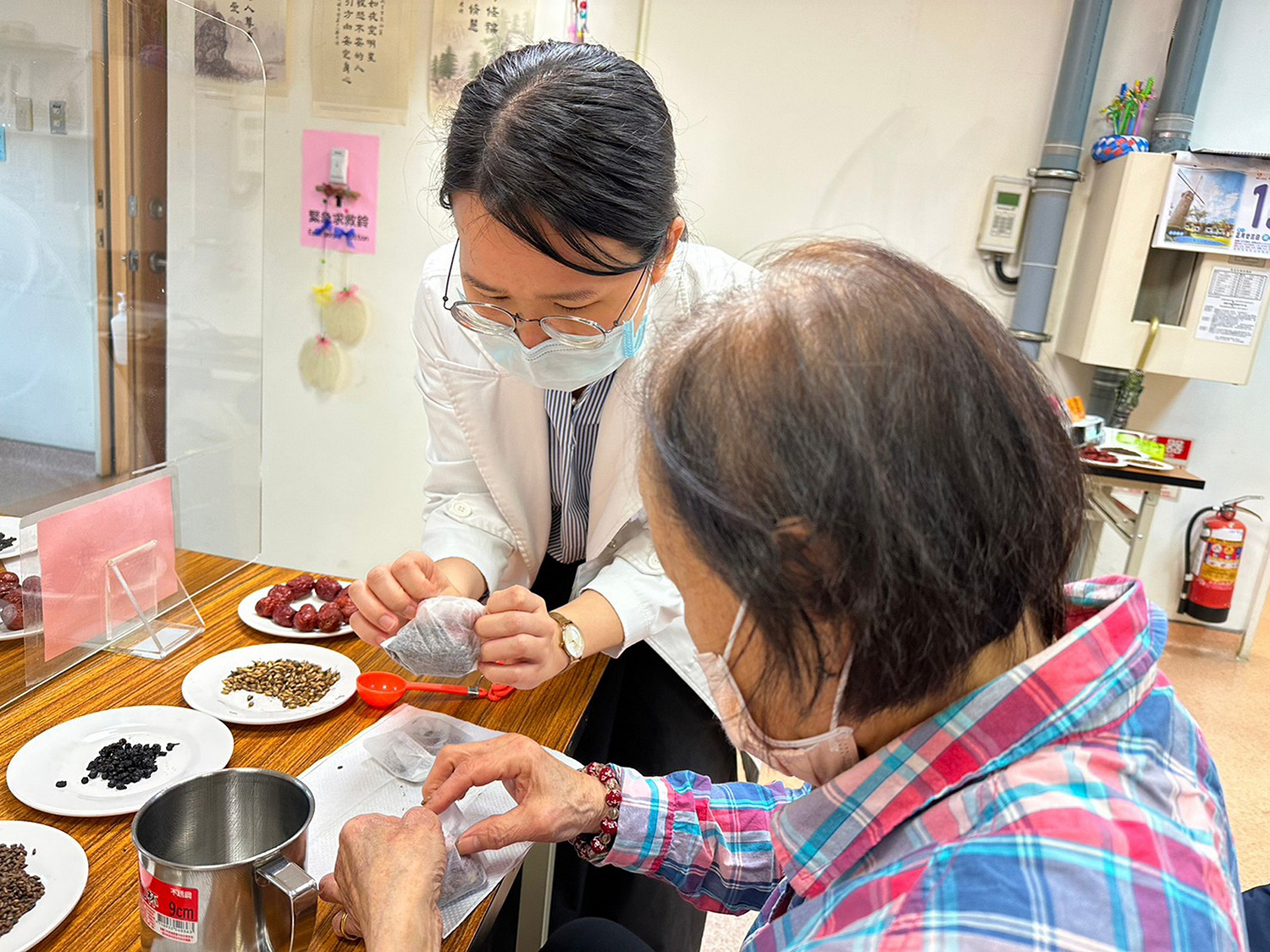 鄭宇真醫師（左）為長輩示範將藥材裝入茶袋中。