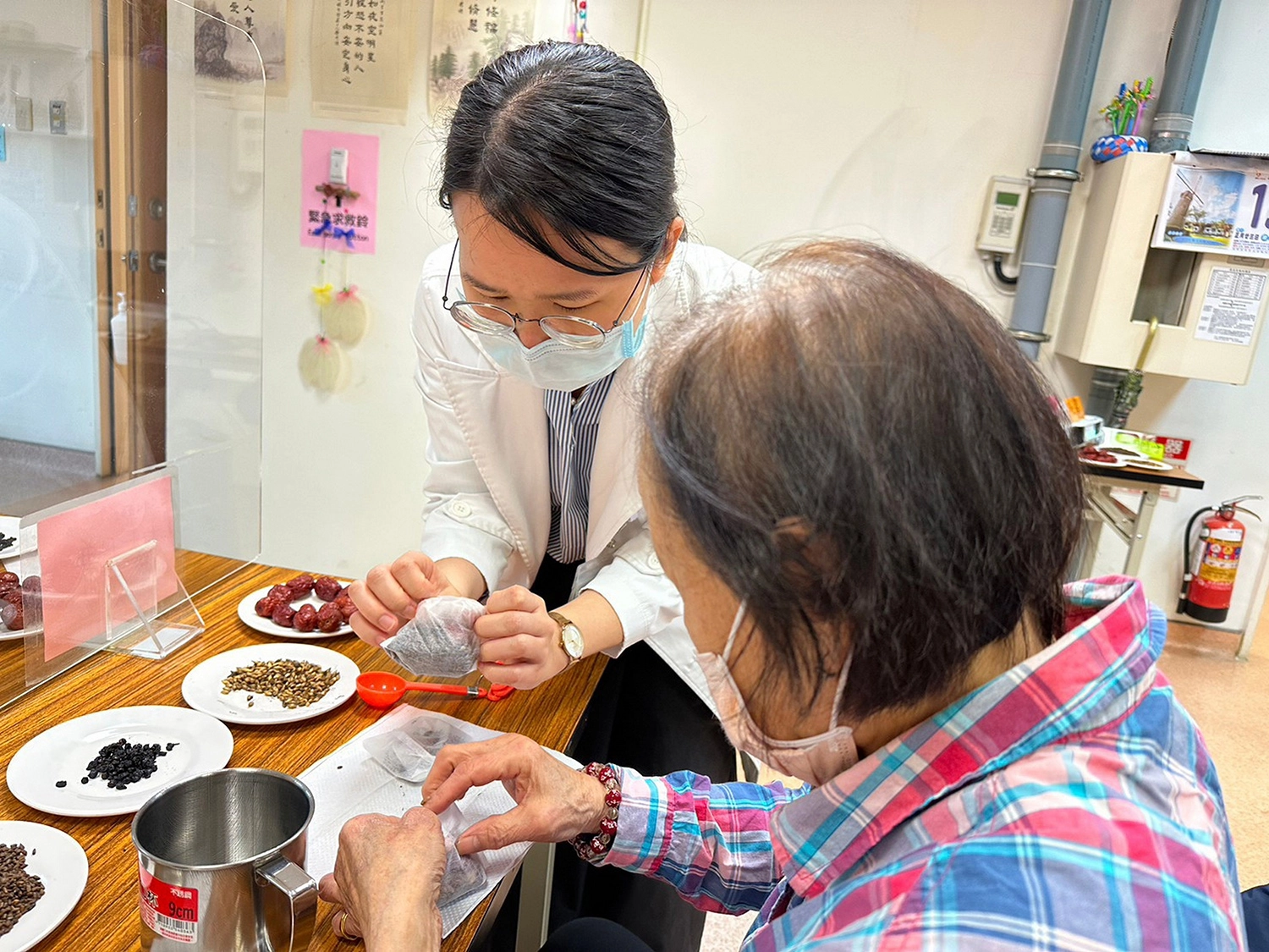 鄭宇真醫師（左）為長輩示範將藥材裝入茶袋中。