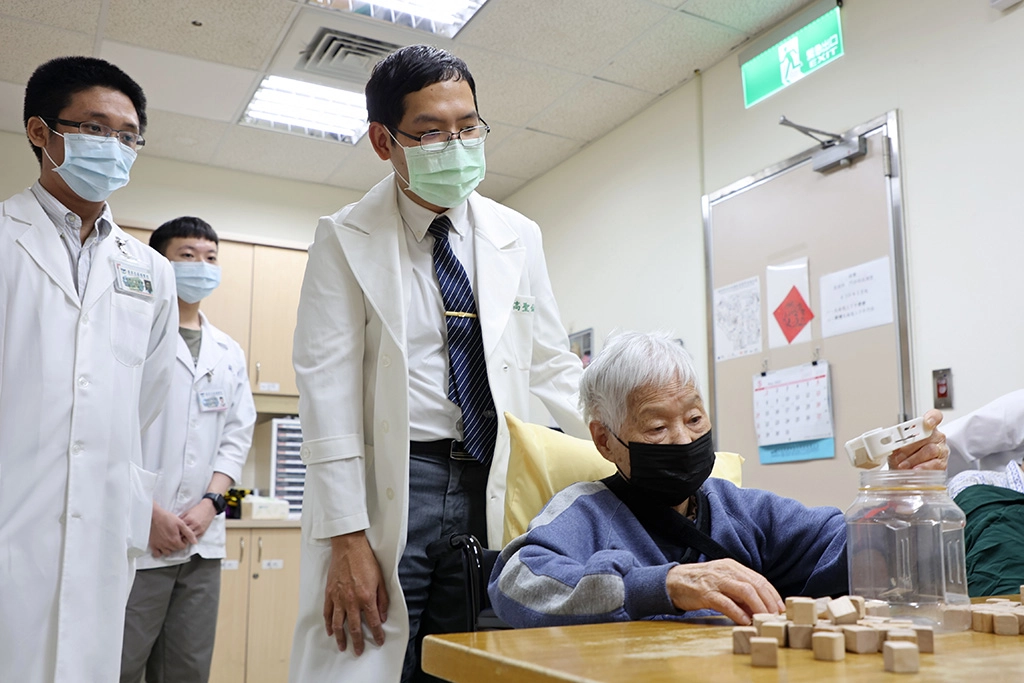 楊奶奶積極復健，練習單手用夾子將積木夾起並放入桶內。