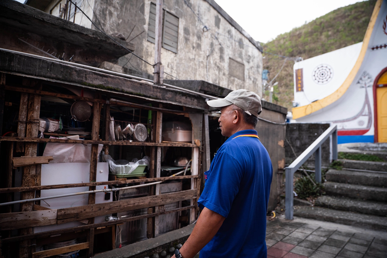 住在椰油部落的阿佳，家外牆被解體剝落，從室外就能看見家中馬桶和廚房。圖為阿佳爸爸檢視遭颱風破壞的房屋 (台灣世界展望會提供) 