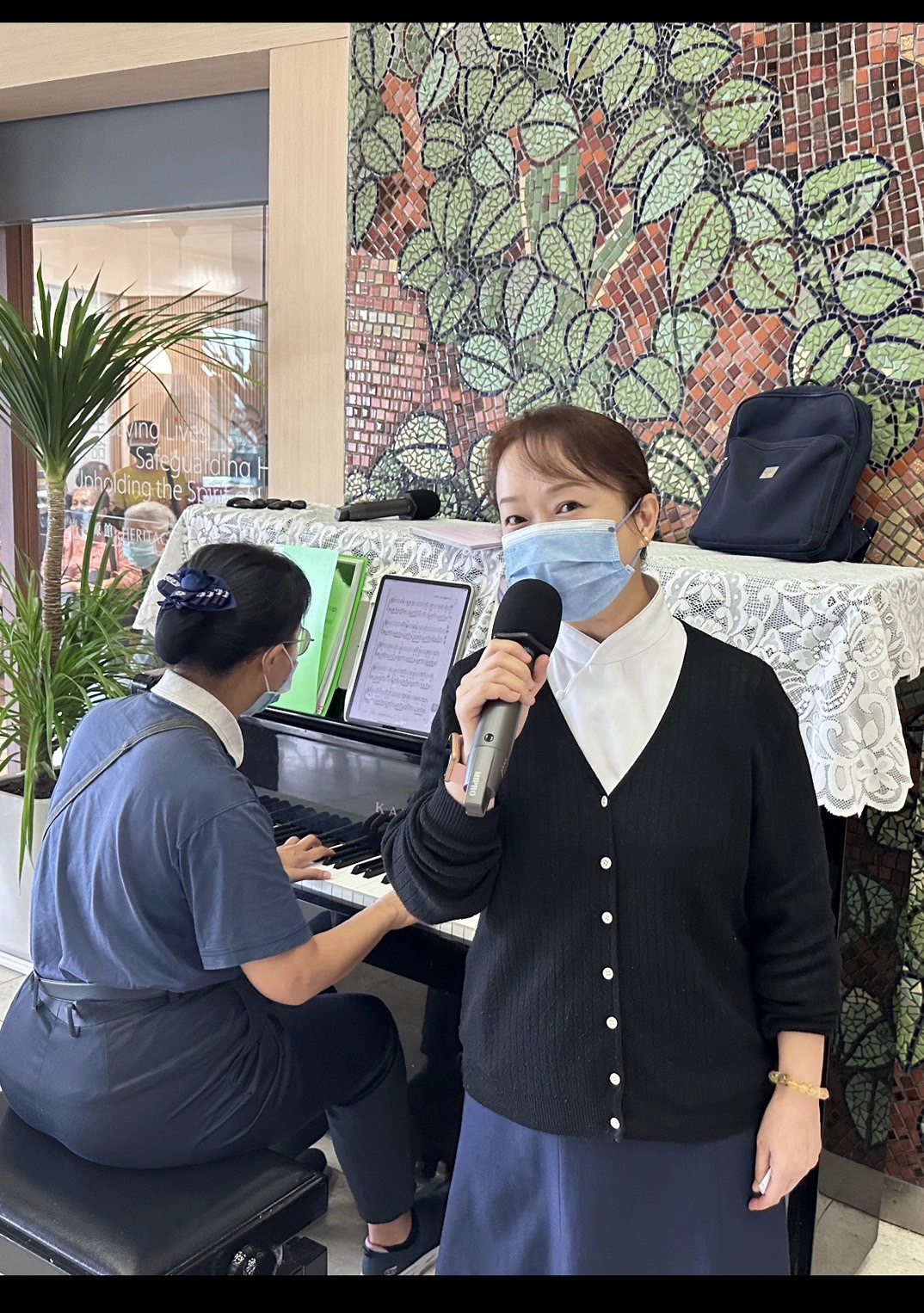 志工陳蓉珍(左，彈鋼琴者)、黃靖惠在大廳分別彈奏、演唱「月亮代表我的心」，吸引許多病友、家屬隨旋律一起唱和。