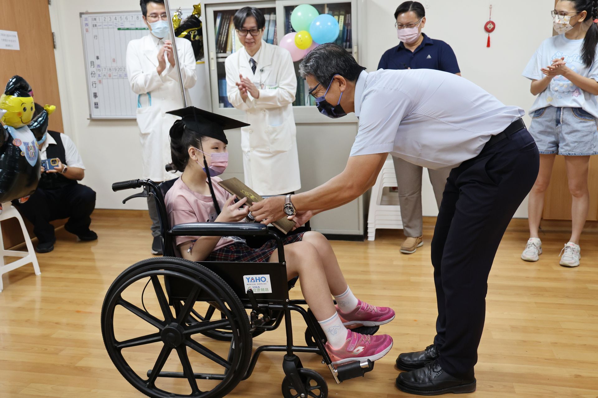 明義國小校長許傳德頒發畢業證書祝賀黃小妹從學校畢業，也從病房畢業，學校導師與師長也一起送上祝福。