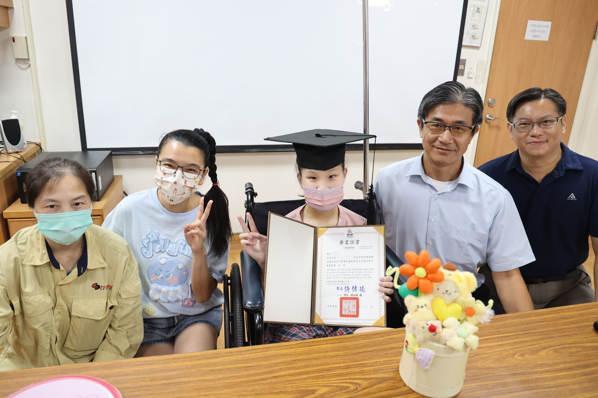 明義國小校長許傳德頒發畢業證書祝賀黃小妹從學校畢業，也從病房畢業，學校導師與師長也一起送上祝福。