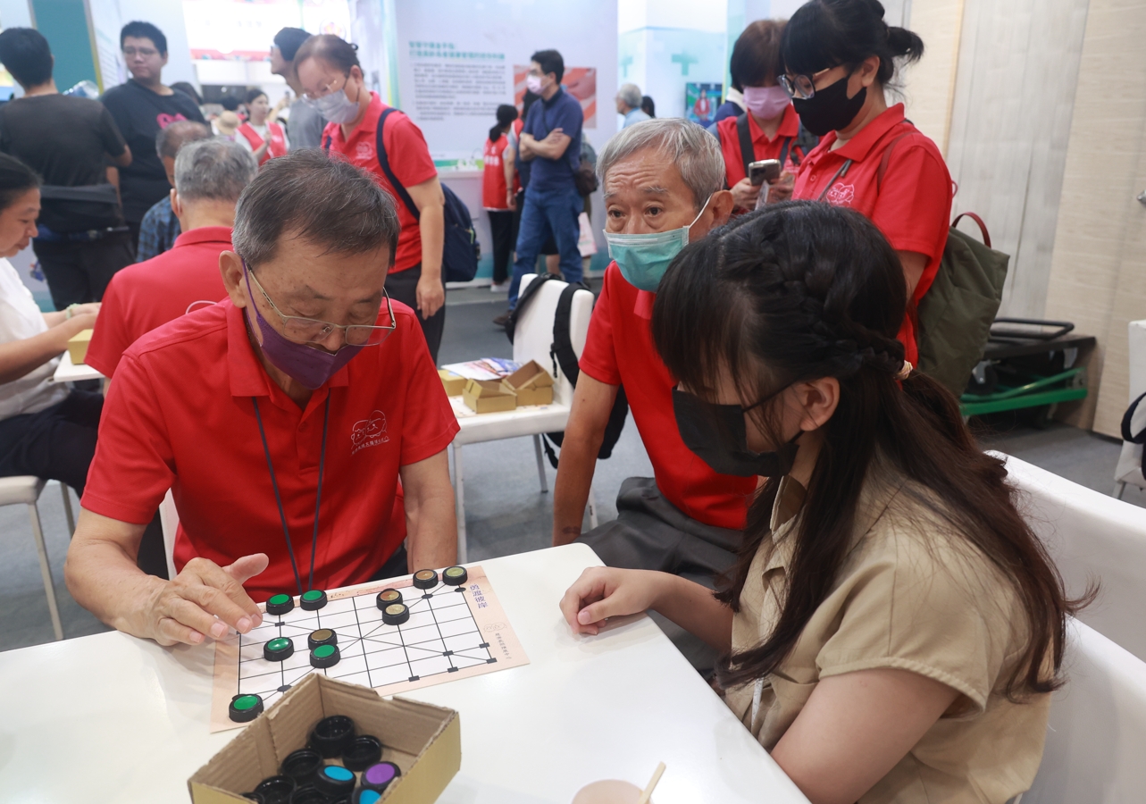 五位失智長者(穿紅衣)及陪同者，展現失智症者練習的成果和讓他們承擔桌長，帶動與會民眾玩環保桌遊。