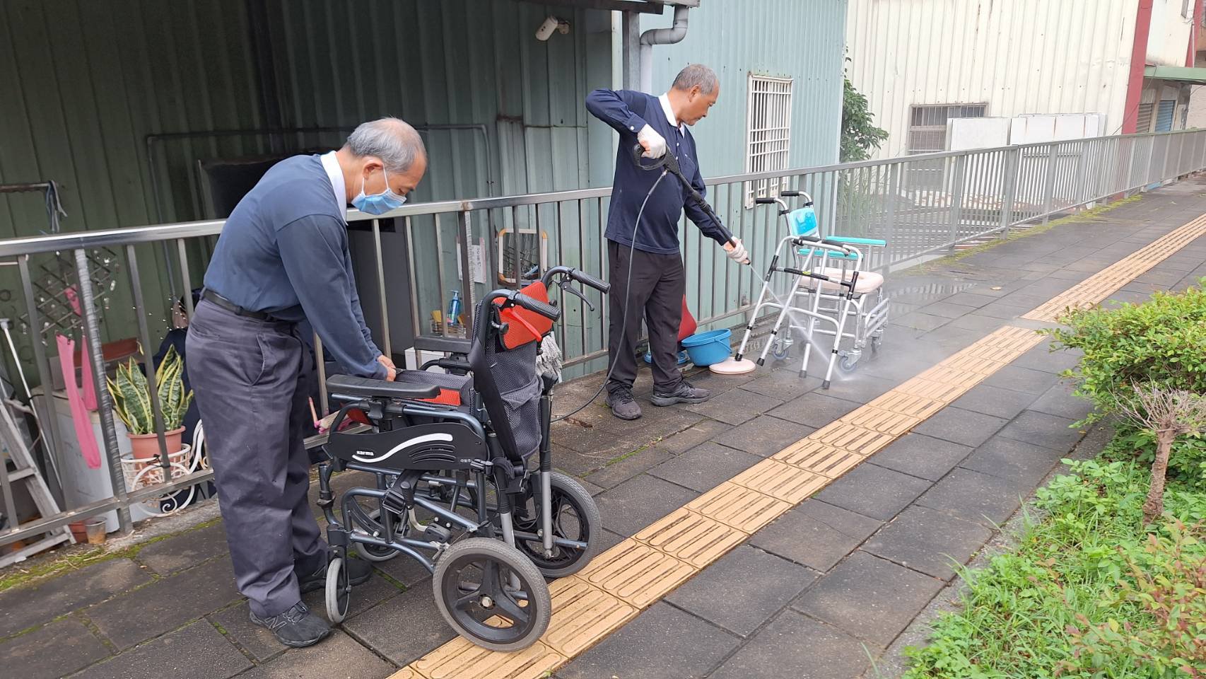 志工蘇國棟（右）將載回來的輔具用洗車的噴槍大力沖洗，做徹底清洗消毒，他表示有做就有福。黃中萬（左）把回收回來的輪椅被套也一起清洗消毒。