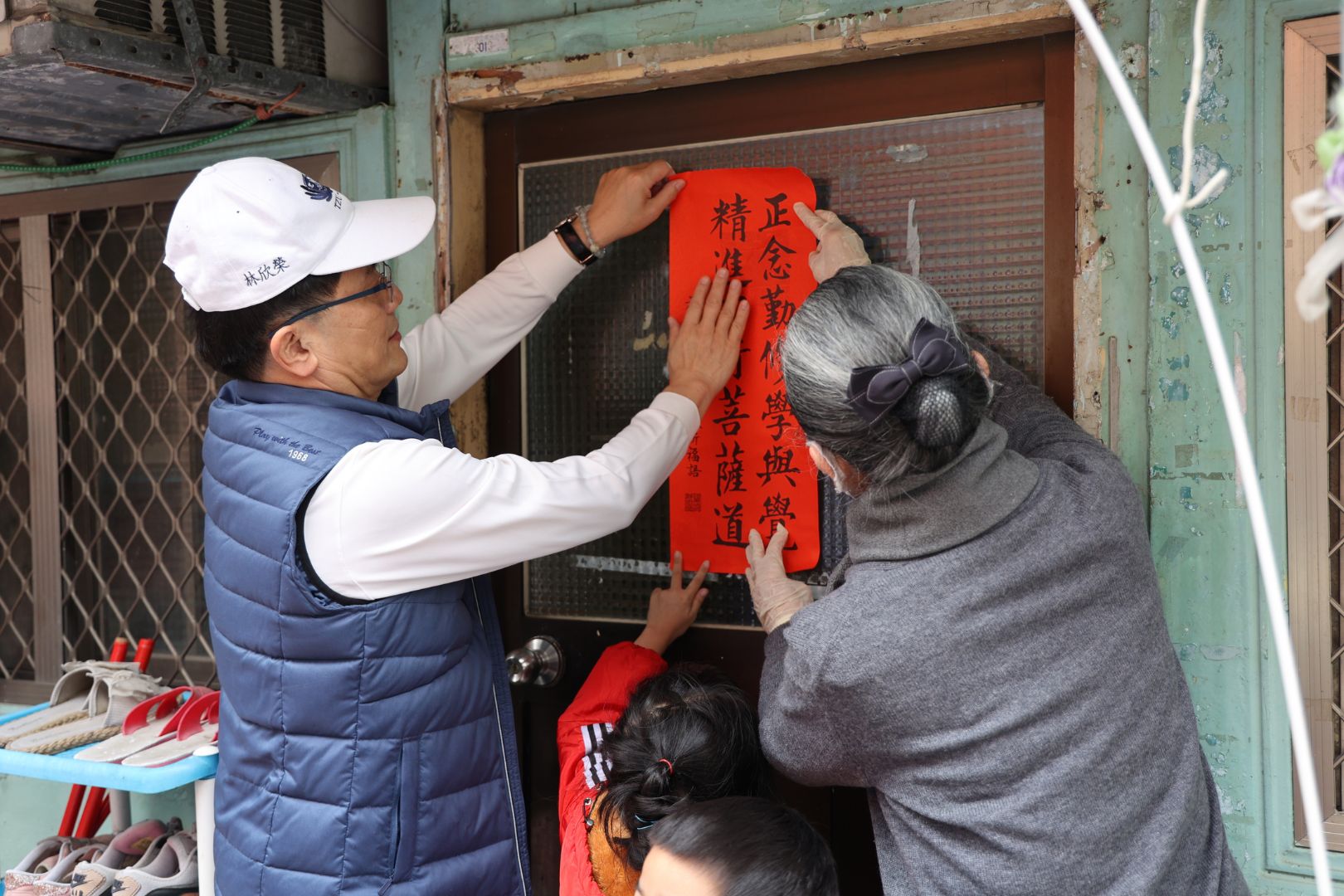 林欣榮院長(左)、顏惠美主任(右)與高先生的女兒(中)一同開心地貼上春聯，為高先生一家送上新春祝福。