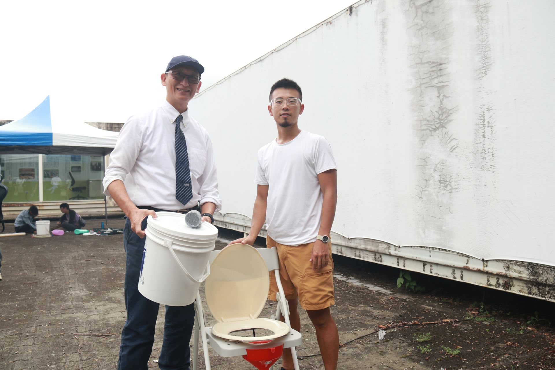 學員自己到大賣場買材料製作屬於家庭的乾式廁所，學員許博勛他特別選簡單的材料，只要用束帶，美工刀等身邊找的到的工具，就能做一個簡易的防災廁所。(圖為與邱奕儒老師合照)