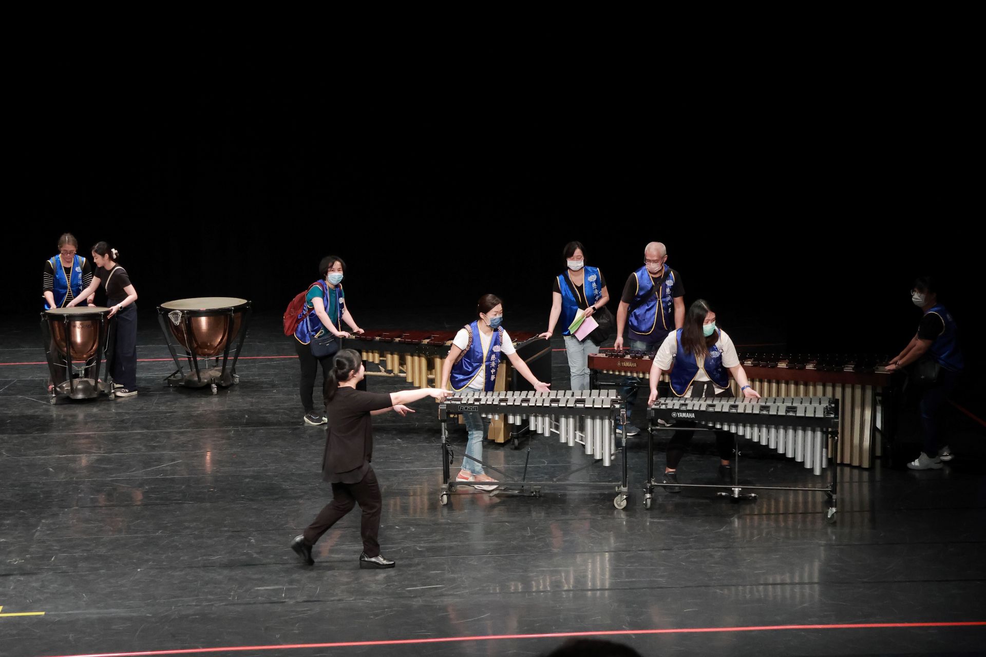 家長志工們在舞台上搬運樂器，動作俐落而有默契。