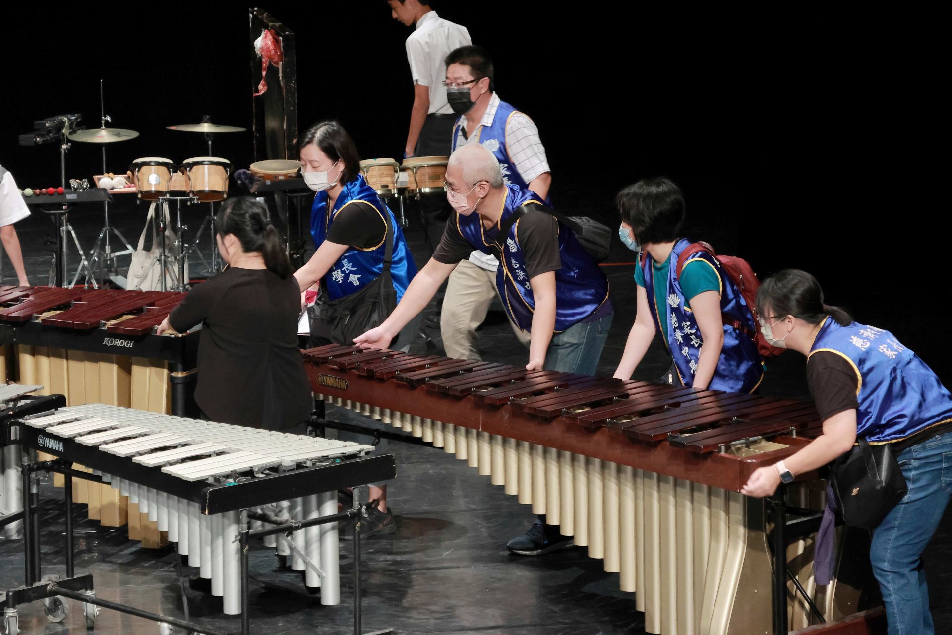 家長們在舞台旁協助搬運與布置樂器，默默成為孩子最可靠的支持力量。