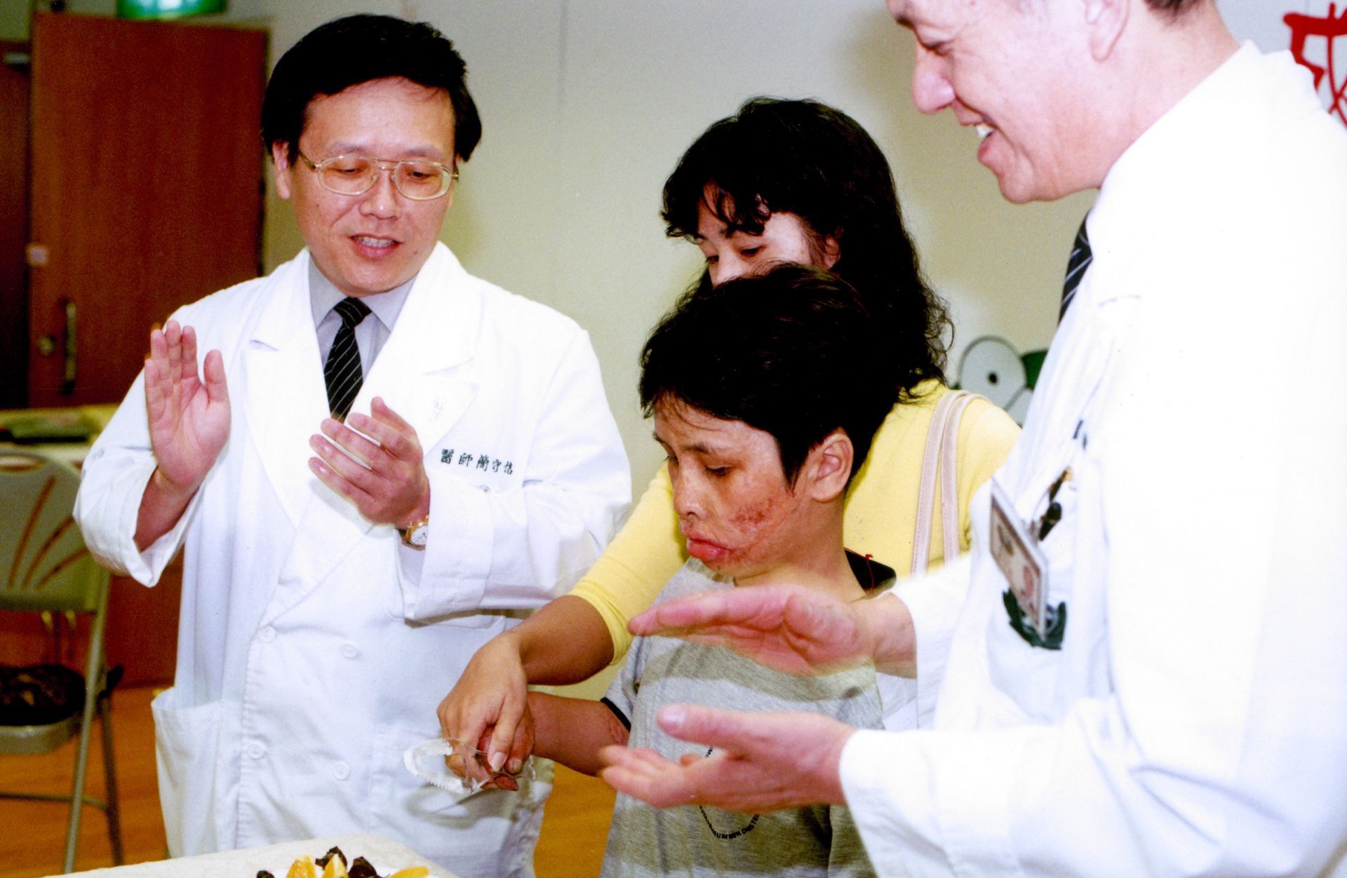 2001年，來自越南的官世成在大林慈濟醫院照顧下恢復走路，在歡送會切下象徵重生的蛋糕。左一為簡守信院長，右一是林俊龍執行長。