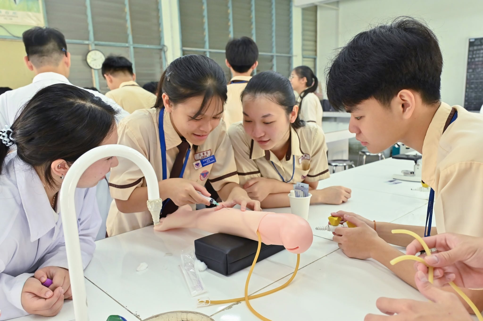 學生專注學習抽血操作,在指導下透過模擬手臂進行實作練習,親手操作。