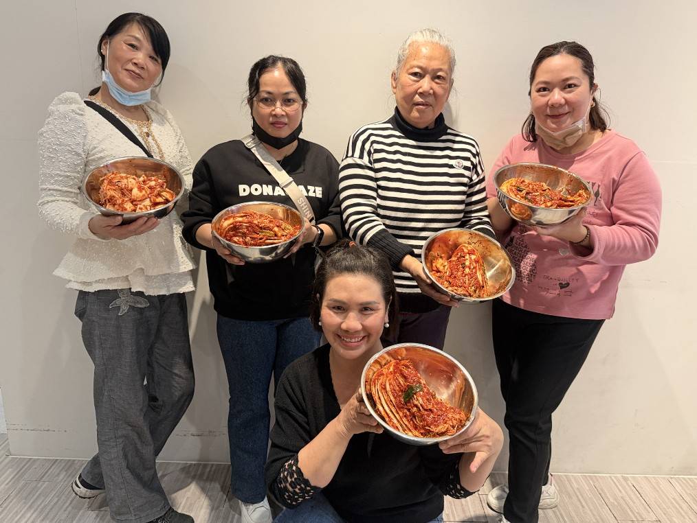  新住民手持親手製作的辛奇泡菜成果合影，象徵多元文化融合與情感交流的美好成果。