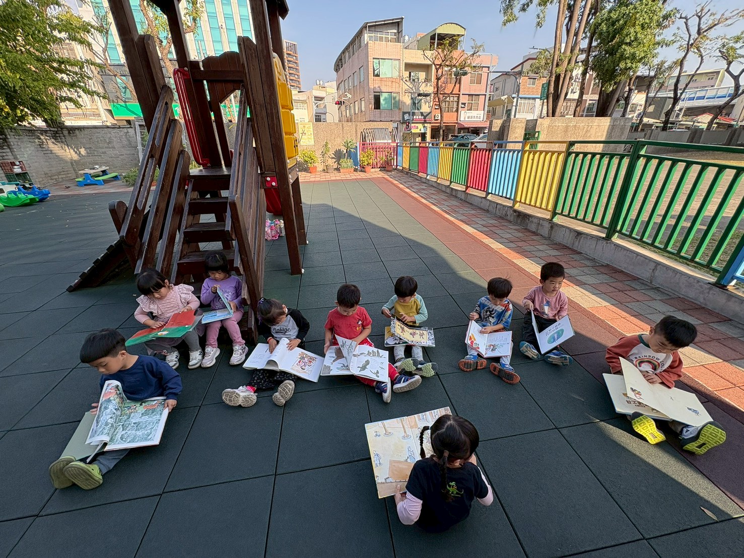 透過行動書車將圖書資源帶入校園,孩子們席地而坐翻閱繪本,在陽光灑落的遊戲場中自在閱讀,專注的神情成為最動人的風景。