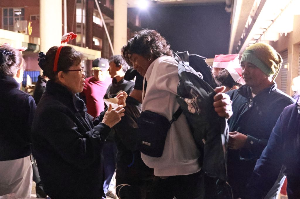  志工貼心地幫忙漁工試穿外套、選好尺寸，讓他們保暖身軀。