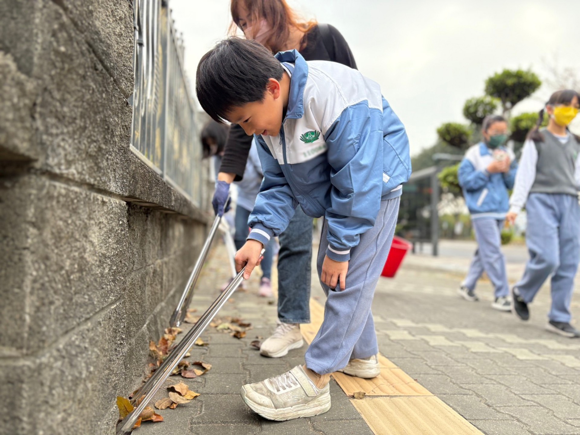學生仔細清理街道死角的落葉與廢棄物。