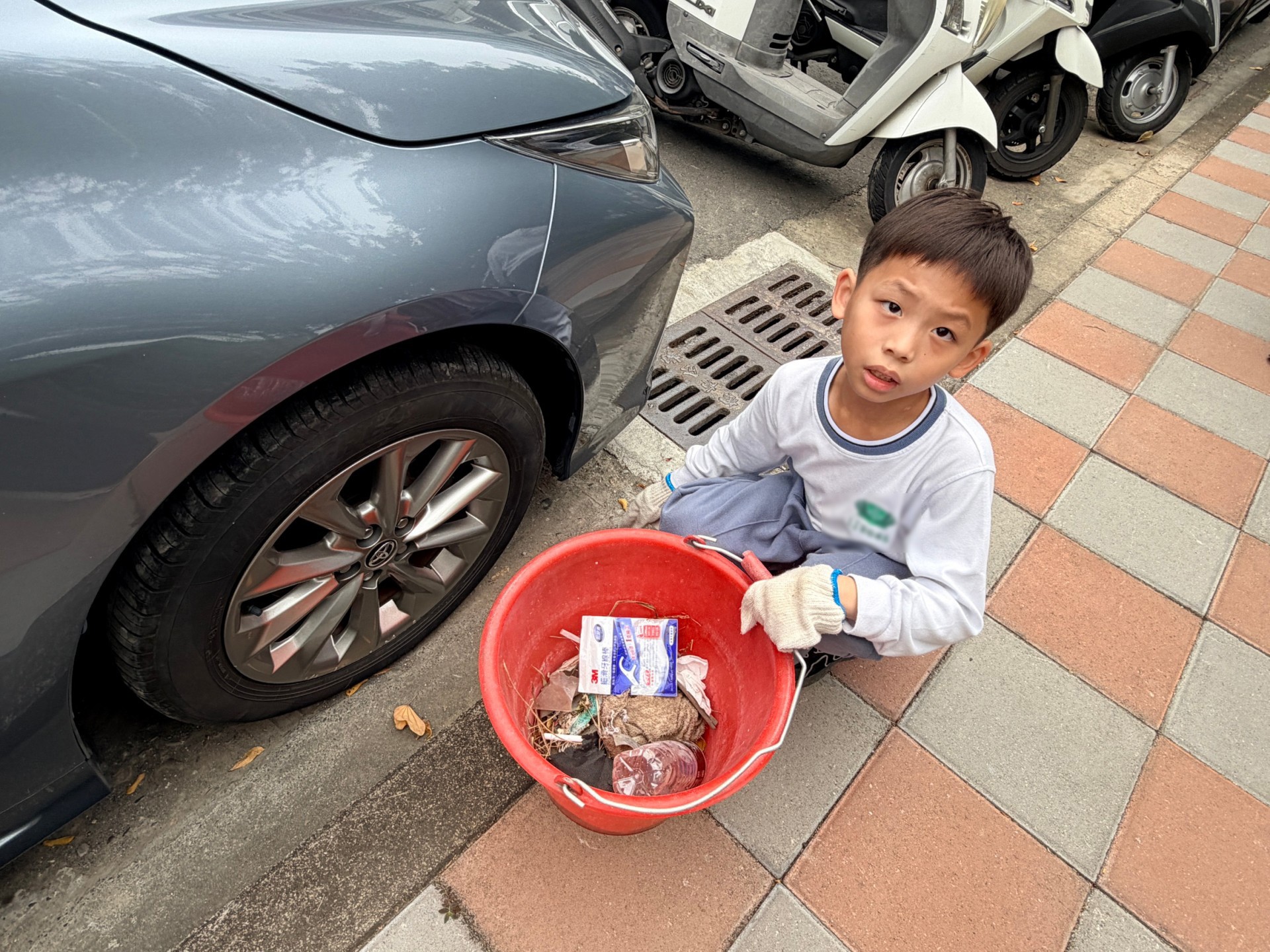 孩子專注撿拾汽車底部的菸蒂，細小紙屑也不放過。