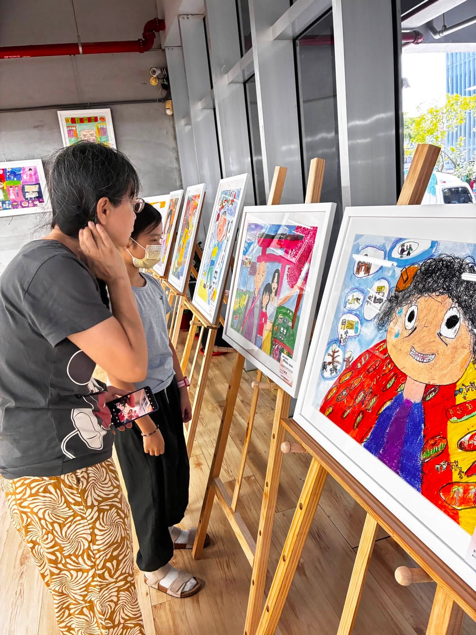 民眾駐足欣賞學生畫作，細細品味每幅作品背後的家庭故事，在觀展過程中感受藝術帶來的感動與跨世代交流的美好。
