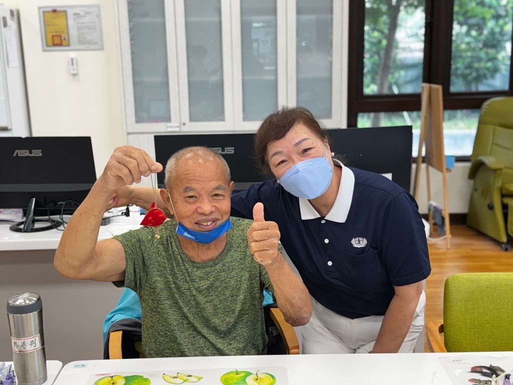 陪伴長者的志工沈碧鳳(右)有感而發地說：「阿公阿嬤來到日照中心，不僅能和大家聊天互動，還能動手學東西、做健康操，生活多了很多樂趣。」