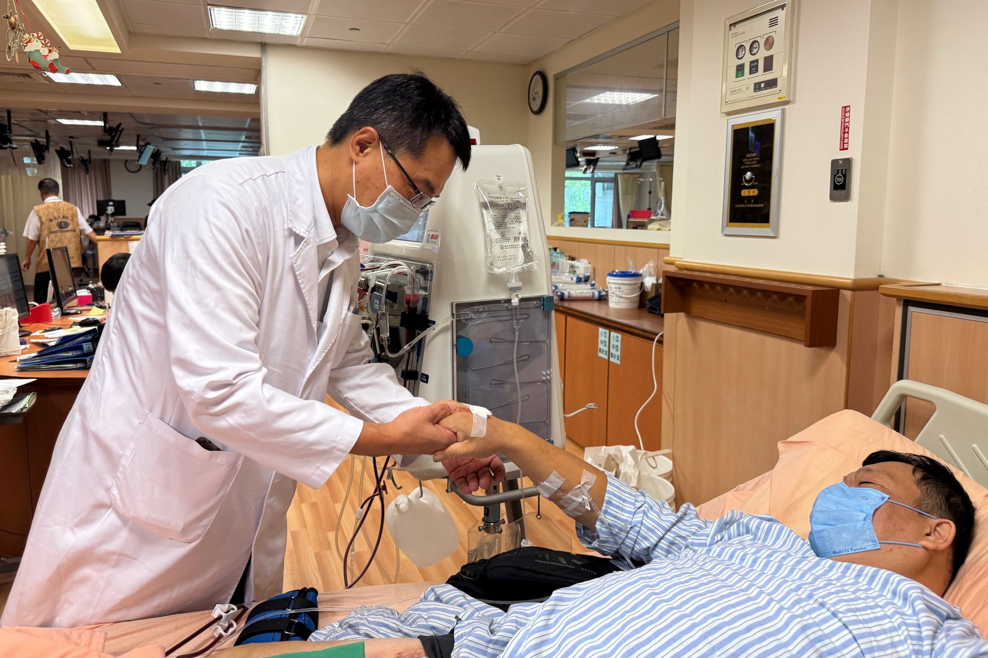 楊洵醫師（左）檢視張先生（右）接受血漿置換術的血管通路情形。