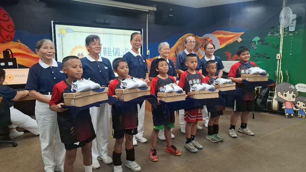 在志工吳雅玲引導下，十二位小朋友分組上台接受球鞋。志工們將鞋子一雙雙放進孩子手中，也將滿滿祝福送進孩子心裡，期待他們穿著新鞋，在球場上勇敢奔跑、奮力拚搏。