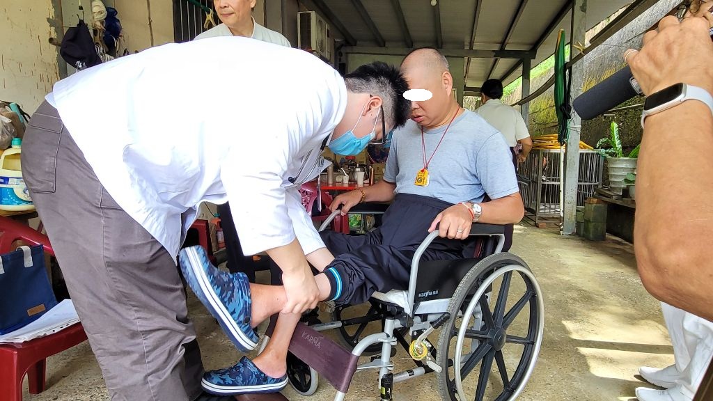 鄉親謝先生(右)因為意外以致無法行走，楊崴光醫師(左)檢查謝先生的雙腳肌力，評估復健雙腳恢復行走能力的可能。