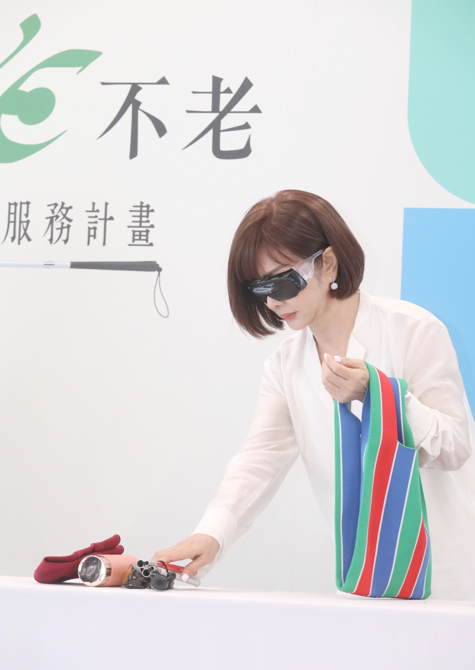 愛盲基金會年度代言人陳美鳳在記者會上戴上視覺模擬眼鏡進行闖關,找出水果擺盤和日用品